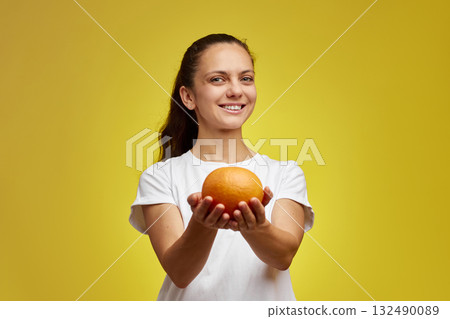 Happy Caucasian woman holds grapefruit isolated on yellow background Happy Caucasian woman holds grapefruit isolated on yellow background 132490089