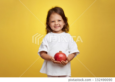 cute little child girl holding a pomegranate on yellow background. 132490090