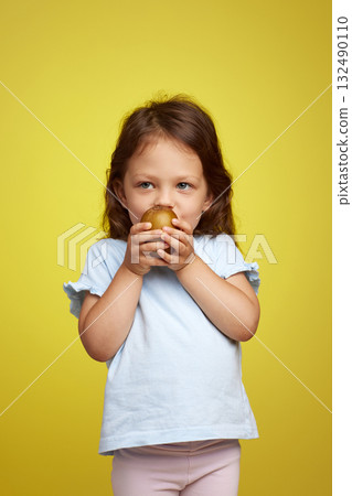 cute Caucasian little child girl holding kiwi fruit on yellow background cute Caucasian little child girl holding kiwi fruit on yellow background 132490110