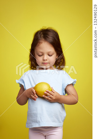 cute Caucasian little child girl holding lemon on yellow background 132490129