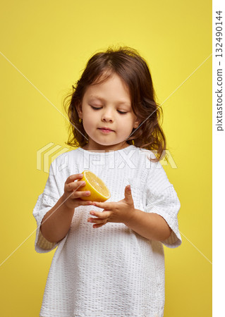cute Caucasian little child girl holding lemon on yellow background 132490144