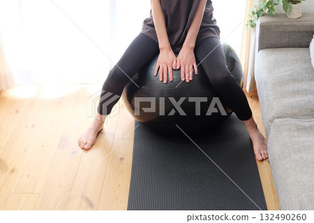 A woman in her 40s sitting on a balance ball A woman in her 40s sitting on a balance ball 132490260