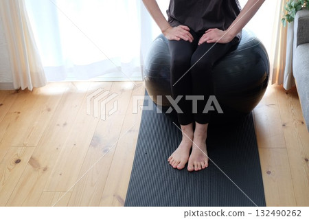 A woman in her 40s sitting on a balance ball A woman in her 40s sitting on a balance ball 132490262