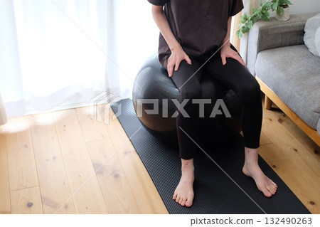 A woman in her 40s sitting on a balance ball A woman in her 40s sitting on a balance ball 132490263