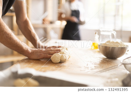 Baker's hands kneading raw dough in bakery 132491395
