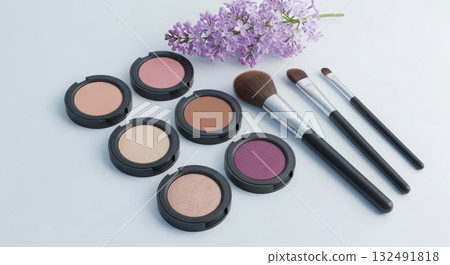 Cosmetic set with eyeshadow palette and makeup brushes on a light background, complemented by a delicate lilac sprig. 132491818