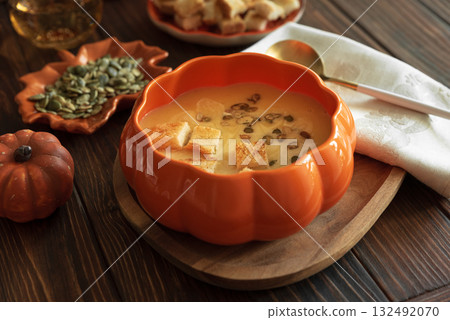 Creamy pumpkin soup with croutons and seeds, served in a pumpkin-shaped bowl on dark wooden table. 132492070