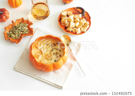 Creamy pumpkin soup with croutons and seeds, served in a pumpkin-shaped bowl on white wooden table. Top view 132492075