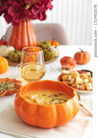 Creamy pumpkin soup with croutons and seeds, served in a pumpkin-shaped bowl on white wooden table. Creamy pumpkin soup with croutons and seeds, served in a pumpkin-shaped bowl on white wooden table. 132492076