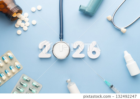 2026 Happy New Year banner for health care and medical concept. Stethoscope with doctor pills, syringe, vaccine vial, eyes drop, antibiotics and white number 2026 on table blue background. 2026 Happy New Year banner for health care and medical concept. Stethoscope with doctor pills, syringe, vaccine vial, eyes drop, antibiotics and white number 2026 on table blue background. 132492247
