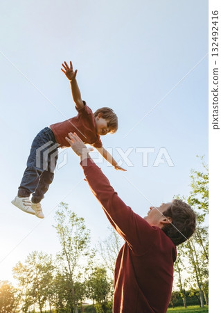Father throwing son in the air outdoors 132492416