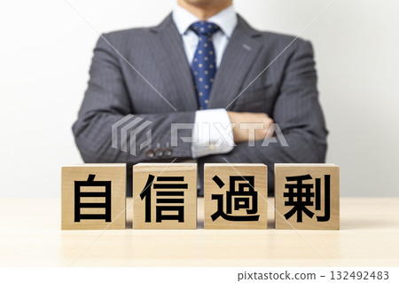 一名商人雙手交叉，身旁有一塊寫著「過度自信」的方塊 132492483