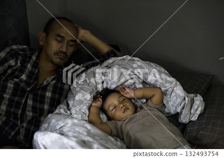 Dad Sleeping Beside Young Child In Daytime, A peaceful dad naps beside a young child, soft sunlight warming the cozy scene, perfect for a family photography shot or a tender bonding showcase. 132493754