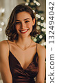 Smiling young Caucasian woman with short brown hair, wearing a dark dress, in front of a decorated Christmas tree with soft lights, celebrating New Year 2026. 132494042