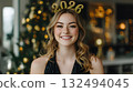 Smiling young Caucasian woman with long wavy hair wearing a black dress and a 2026 headband. Christmas tree and festive lights in the background. 132494045