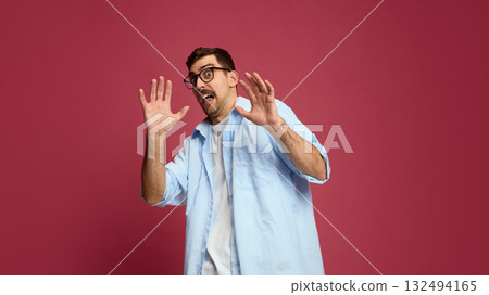 Frightened man raising hands in defensive gesture with scared expression Frightened man raising hands in defensive gesture with scared expression 132494165