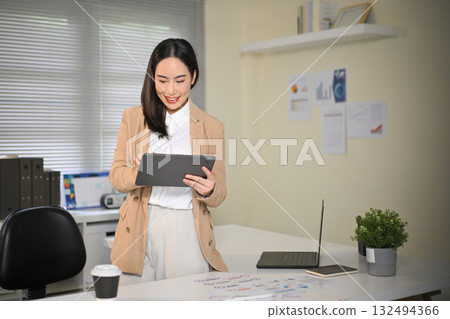 Smiling businesswoman in modern office using tablet to review charts and data, showing confidence and satisfaction with work progress Smiling businesswoman in modern office using tablet to review charts and data, showing confidence and satisfaction with work progress 132494366