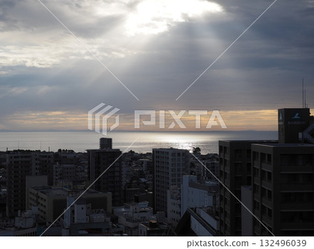 Sunset view of the sea and cityscape with rays of light shining through the cloudy sky 132496039