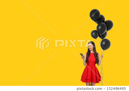 Woman in red dress holds black balloons and uses smartphone 132496495