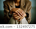 A woman is sitting with her hands on her lap, wearing a ring on her left hand 132497275