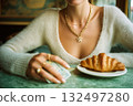 A woman is sitting at a table with a croissant and a stack of bills 132497280