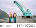 Two men are standing next to a large green crane 132497281