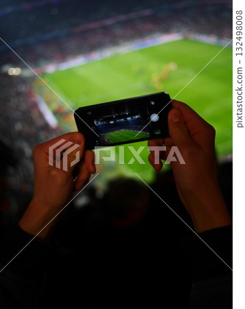 Person is holding a cell phone and taking a picture of a soccer field 132498008