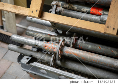 Stack of metal scaffolding parts stored with wooden planks above creates industrial composition. Scratched steel surfaces show signs of use and construction work preparation 132498181