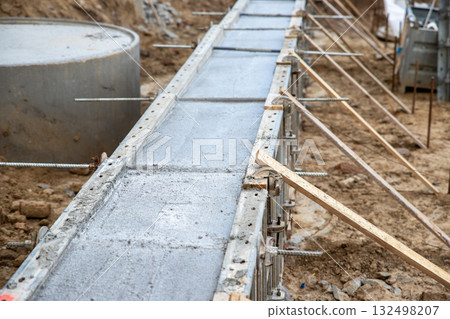 Concrete foundation poured into metal formwork at construction site. Steel rods, braces and rebar elements create strong structure supported by soil and wooden beams 132498207