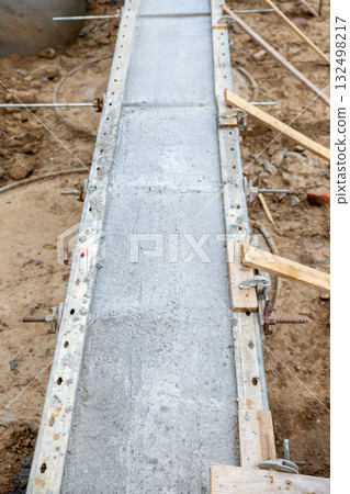 Concrete foundation poured into metal formwork at construction site. Steel rods, braces and rebar elements create strong structure supported by soil and wooden beams 132498217