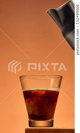 Coffee in glass with rich swirl texture and metal pitcher above against warm background 132499006