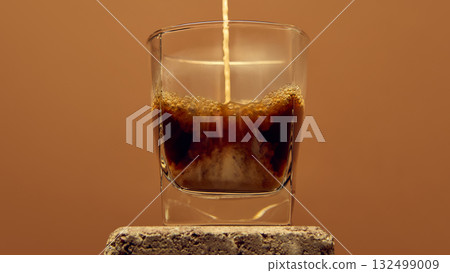Espresso stream pouring into glass with foam forming on top against warm brown background Espresso stream pouring into glass with foam forming on top against warm brown background 132499009