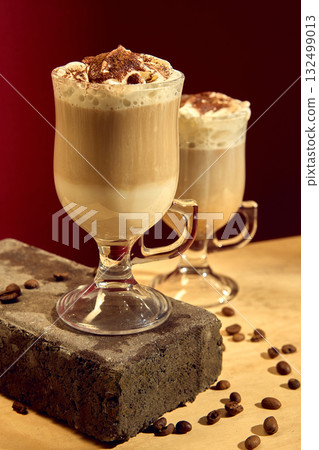 Latte with whipped cream and cocoa powder topping in glass cup with roasted coffee beans Latte with whipped cream and cocoa powder topping in glass cup with roasted coffee beans 132499013