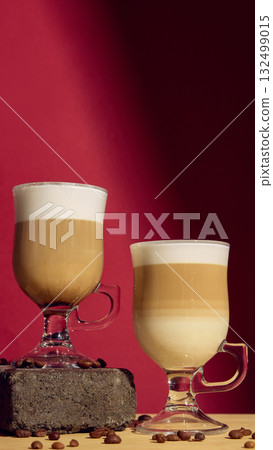 Two layered latte macchiato glasses on red background with roasted coffee beans 132499015