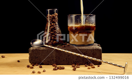 Milk poured into iced coffee with roasted beans and spoon on dark minimalist setup Milk poured into iced coffee with roasted beans and spoon on dark minimalist setup 132499016