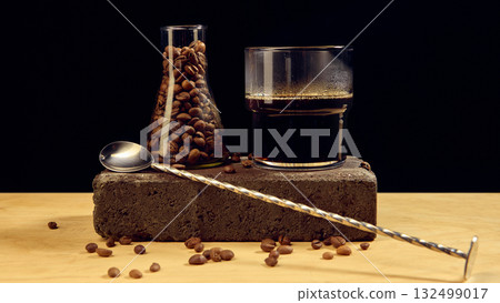 Black coffee and roasted beans in glass container with spoon on dark background minimal composition Black coffee and roasted beans in glass container with spoon on dark background minimal composition 132499017