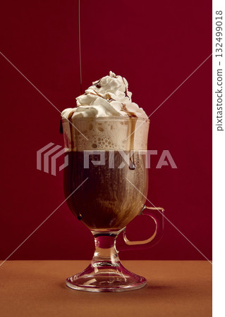 Coffee with whipped cream and chocolate syrup drizzle in clear glass against red background Coffee with whipped cream and chocolate syrup drizzle in clear glass against red background 132499018