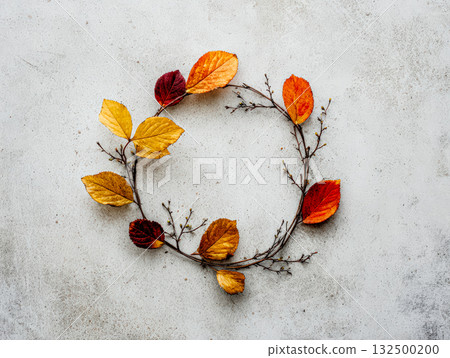Autumn leaves arranged in a circular wreath on a textured concrete background 132500200