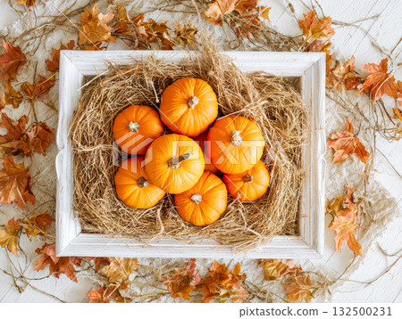 Vibrant orange pumpkins arranged in a rustic wooden box surrounded by autumn leaves and straw 132500231