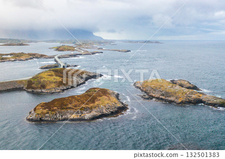 Curving bridges of the Atlantic Ocean Road stretch across small rocky islands, connecting Norways dramatic coastal landscape under cloudy skies. 132501383