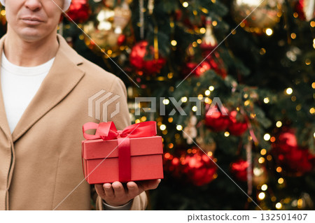 Christmas Red gift box in man hand against Xmas tree. Close up. 132501407