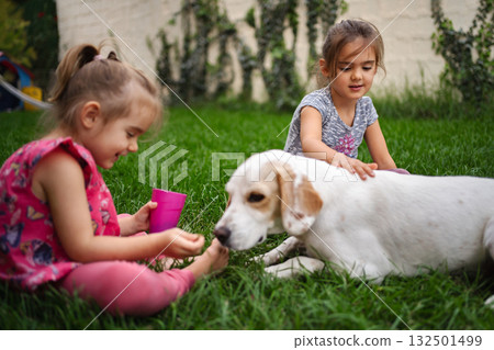 Two joyful girls playing with a friendly dog in a vibrant garden 132501499