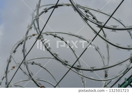 Razor barbed wire on a strictly guarded facility. Razor wire and durable wired fencing. Concept for prisons, military facilities, and nuclear power plants. 132501723