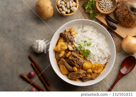Massaman Curry with beef and cooked rice in white plate.Cooked beef meat and potatoes groundnut with massaman curry paste in coconut milk.asian food.Top view. Massaman Curry with beef and cooked rice in white plate.Cooked beef meat and potatoes groundnut with massaman curry paste in coconut milk.asian food.Top view. 132501831