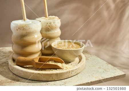Sesame Tahini Latte Delight. Creamy sesame paste and iced tahini lattes on rustic travertine surface. 132501980