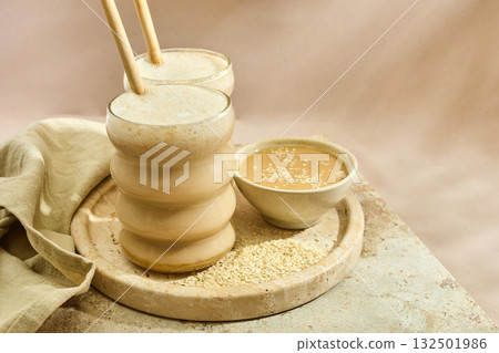 Sesame Tahini Latte Delight. Creamy sesame paste and iced tahini lattes on rustic travertine surface. Sesame Tahini Latte Delight. Creamy sesame paste and iced tahini lattes on rustic travertine surface. 132501986