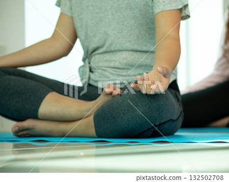 Close-up of a woman practicing meditation in lotus pose on a blue yoga mat indoors. Focus on hand mudra and posture. Concept of mindfulness, inner peace, self-care, and mental clarity 132502708