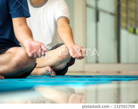 Close-up of two men sitting in a lotus pose during a meditation session indoors. Focus on hands in mudra position. Concept of mindfulness, self-care, mental wellness, yoga practice, and relaxation Close-up of two men sitting in a lotus pose during a meditation session indoors. Focus on hands in mudra position. Concept of mindfulness, self-care, mental wellness, yoga practice, and relaxation 132502709