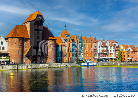 Scenic view of the historic waterfront in Gdansk, showcasing colorful buildings and the medieval crane along the Motlawa River, with vibrant activity from boats and pedestrians 132503150