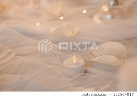 Romantic Soft Focus Candlelight Scene with White Petals and Tulle. Warm Lighting, Wedding Decor, Intimate Mood, Beige and Cream Tones. Romantic Soft Focus Candlelight Scene with White Petals and Tulle. Warm Lighting, Wedding Decor, Intimate Mood, Beige and Cream Tones. 132504017